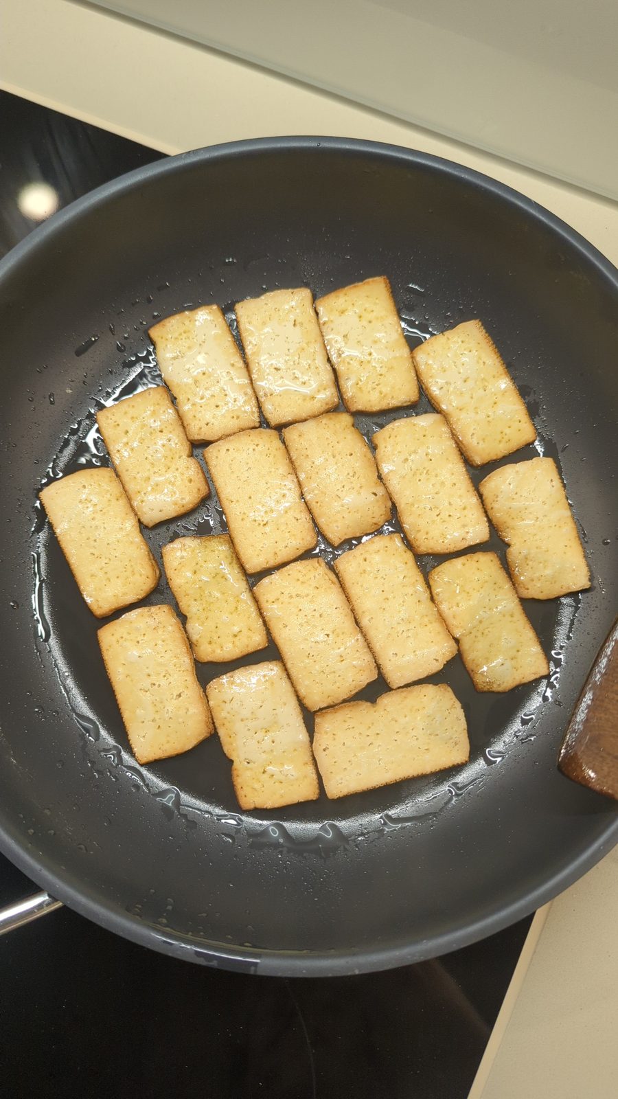 Tofu slices frying in a black pan on a stovetop