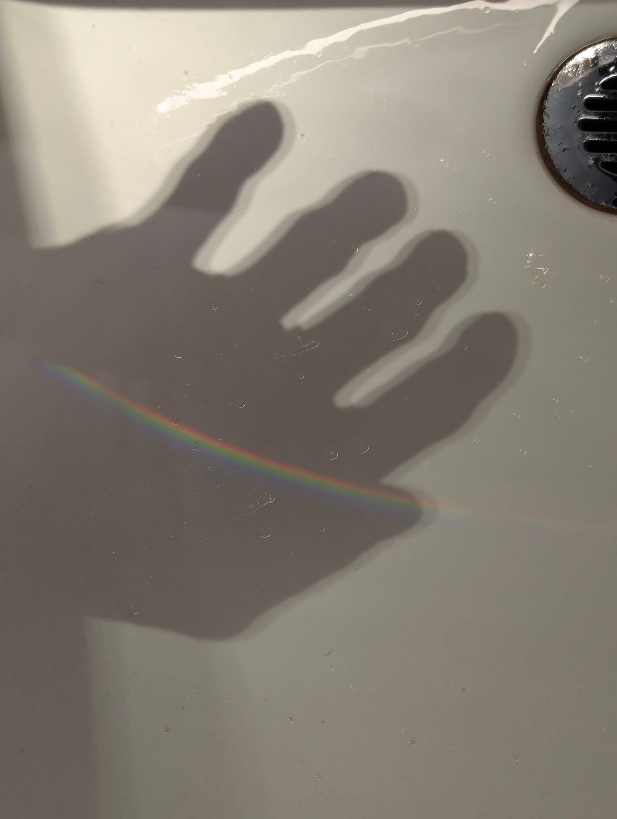 Hand shadow with a small rainbow across a white sink